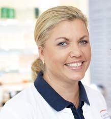 Eine lächelnde Frau in einem weißen Kittel steht in einem hellen, modernen Raum.