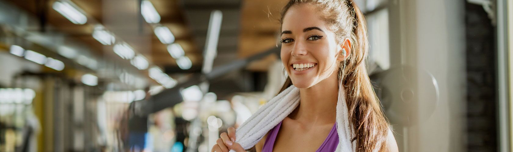 Eine lächelnde Frau mit Handtuch entspannt nach dem Training in einem Fitnessstudio, das Teil unserer Benefits ist.