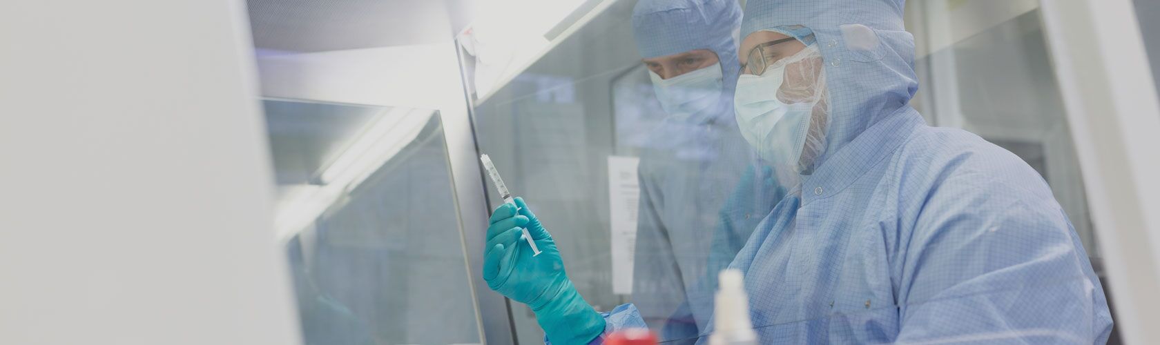 Zwei Wissenschaftler in Schutzanzügen arbeiten konzentriert an einer Qualitätsinitiative im Labor mit einer Spritze.