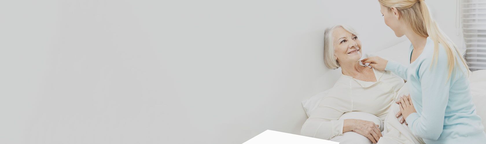 Eine Pflegekraft lächelt, während sie eine ältere Frau im Bett fürsorglich betreut, was auf effektives Wundmanagement hinweist.