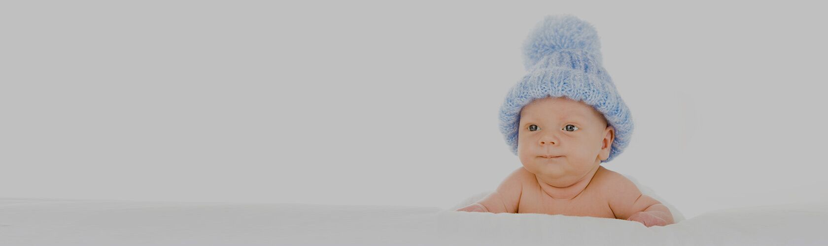 Ein Baby mit einer blauen Strickmütze liegt lächelnd auf einem weißen Hintergrund.