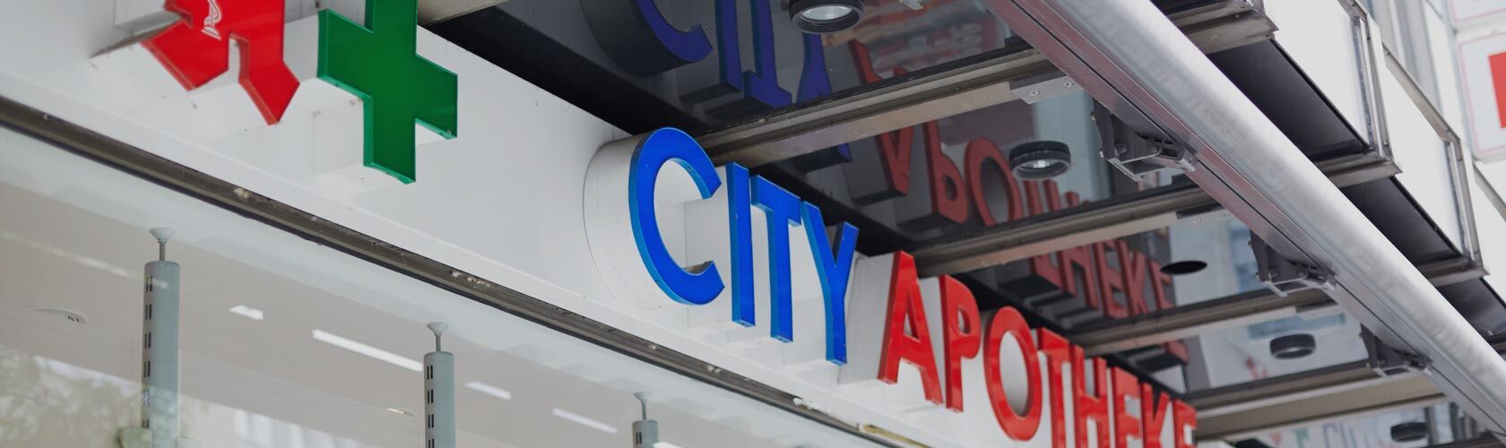 Das Bild zeigt das farbenfrohe Schild einer "City Apotheke" mit einem grünen Kreuz an der Fassade eines Gebäudes.