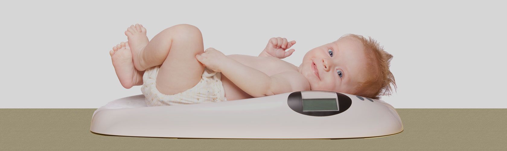 Ein lächelndes Baby liegt auf einer digitalen Babywaage, während es in die Kamera schaut.